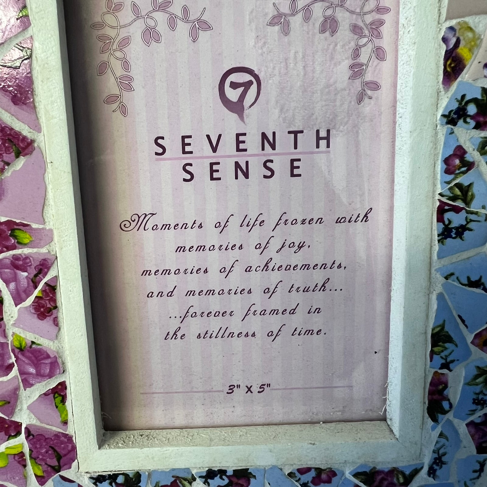 A framed art print featuring the text 'SEVENTH SENSE' with a quote underneath, surrounded by a white distressed frame and a pink floral mosaic border.