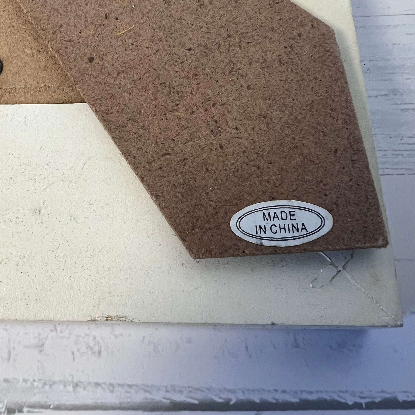 Close-up of a textured brown cardboard or foam sheet layered over a cream-colored surface, with a small oval sticker reading “MADE IN CHINA.”.