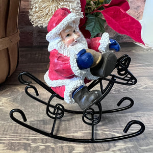 Small Santa Claus figurine on a black wire stand with decorative background