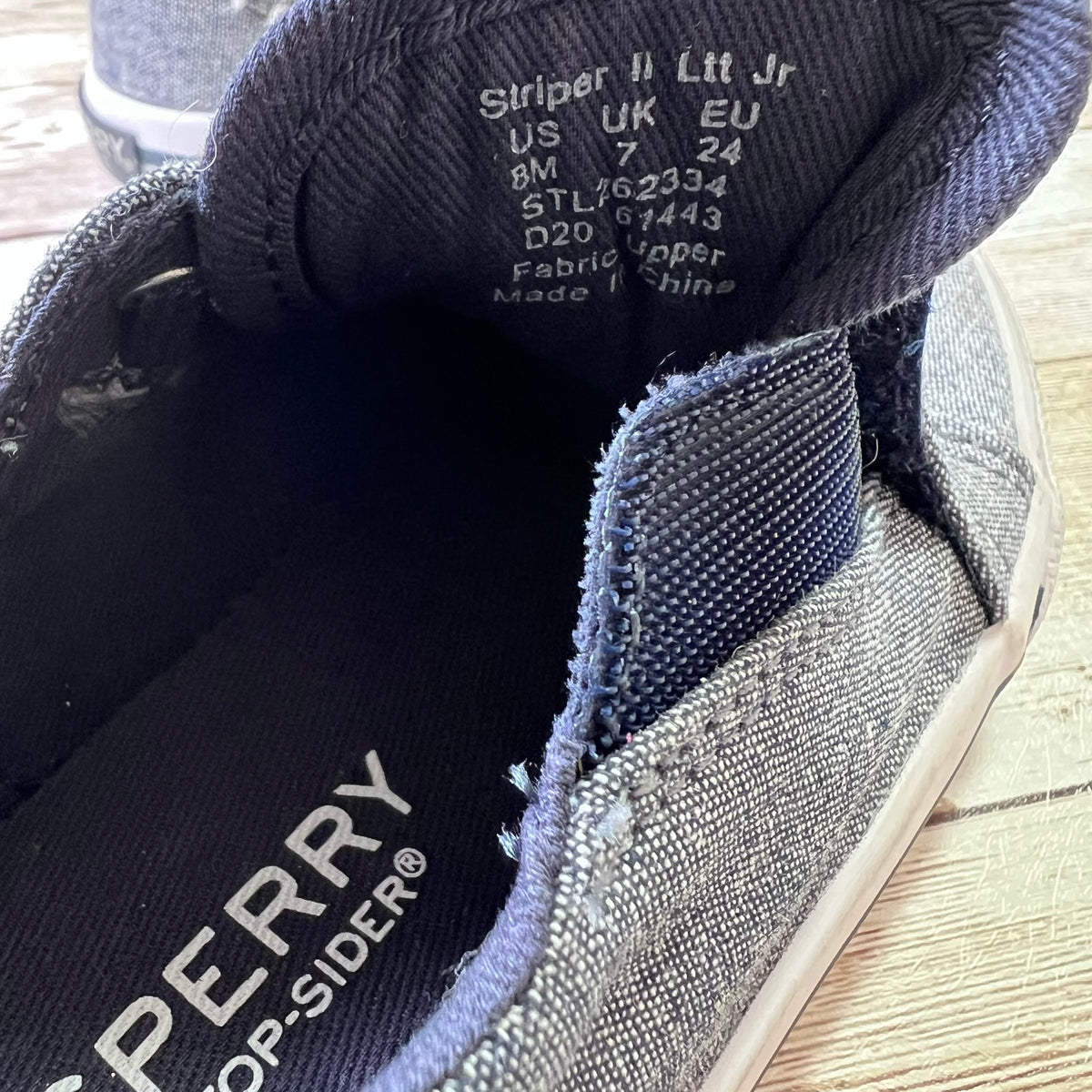 Close-up of a low-top canvas shoe showing the black inner sole with white 'Stripes II Top-Sider' branding and size text, plus the gray fabric upper and dark navy trim.
