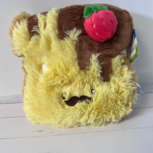 Plush toy resembling a bear with a brown hat and red apple on a white background