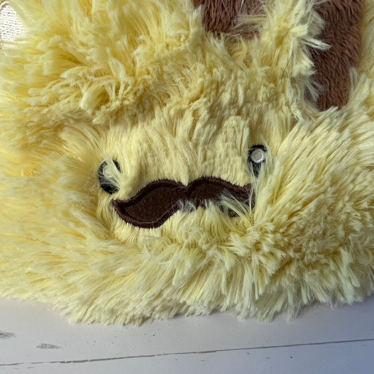 Close-up of a plush toy with a yellow fur texture and a mustache on a white background