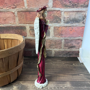 Statue of an angel with a red and gold robe against a brick wall.