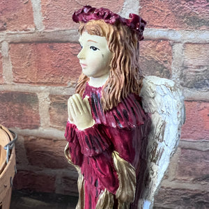 Statue of an angel with a red dress and floral headband against a brick wall.