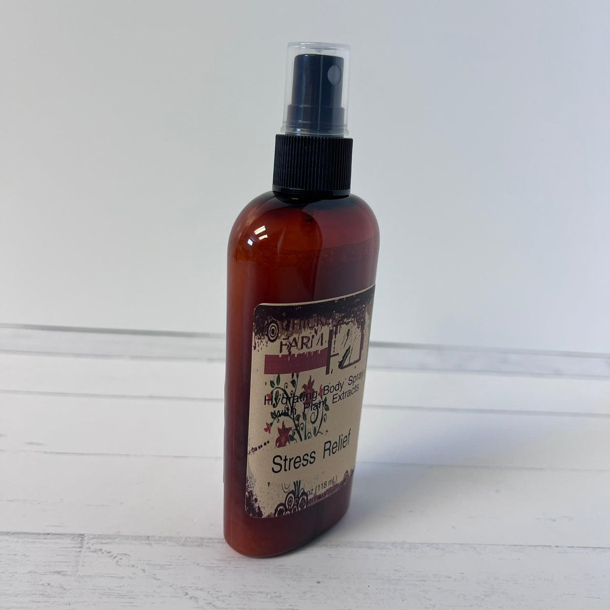 An amber spray bottle Chickenmash Farm Aromatherapy Stress Relief Aromatic Room Spray, standing on a white wooden surface against a white wall.