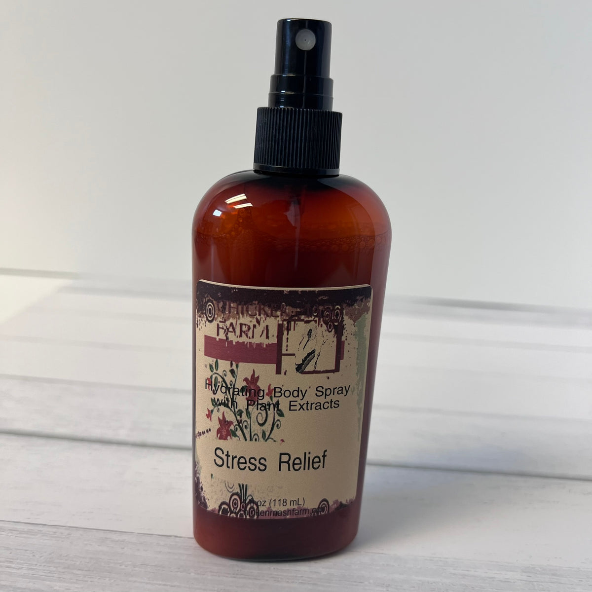 An amber glass spray bottle labeled Chickenmash Farm Stress Relief Body Spray' with a black pump, standing on a light wood surface against a white background.