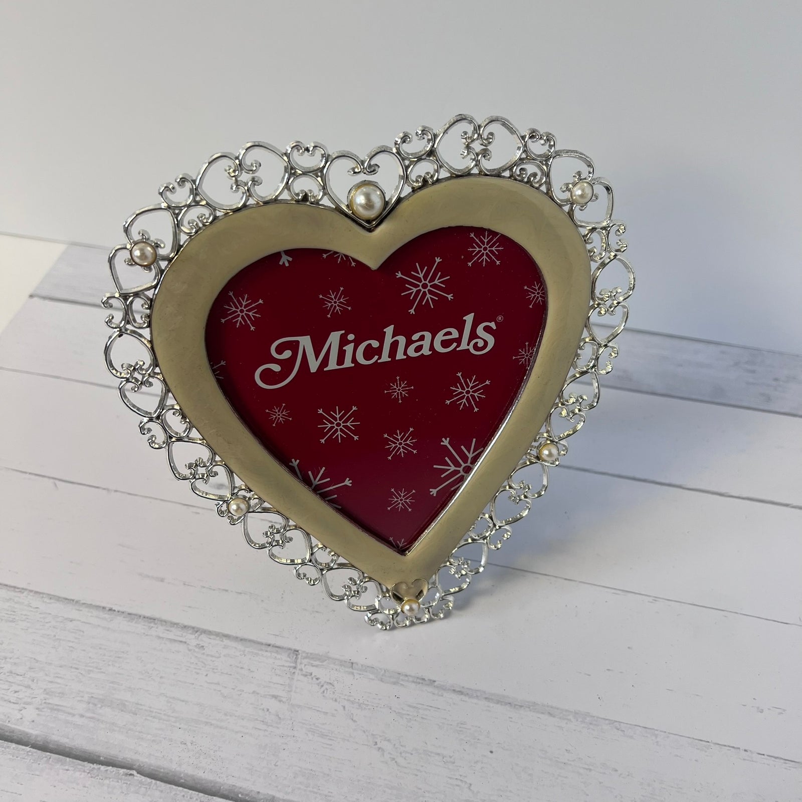 A heart-shaped picture frame with an ornate silver filigree border and a gold-toned center frame. The inner heart is dark red with white snowflake patterns and the name 'Michaels' in white script.