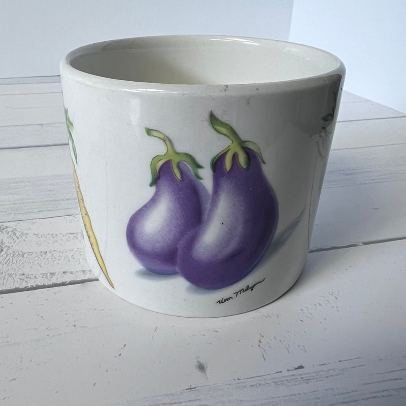 White pot with purple eggplant design on a white wooden surface