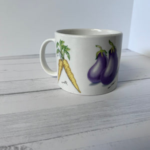 White mug with illustrations of carrots and eggplants on a wooden surface