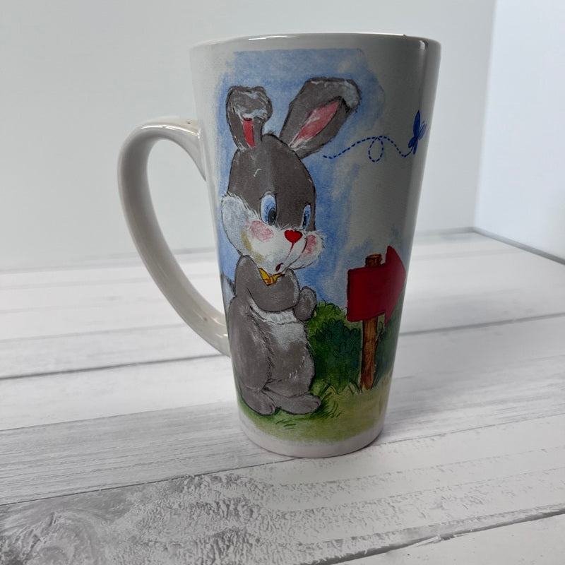 Mug with a painted design of a rabbit and a house on a white wooden surface
