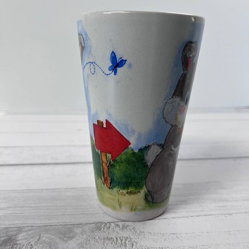 Ceramic mug with a painted design of a red mailbox, blue butterfly, and green field on a white wooden surface.