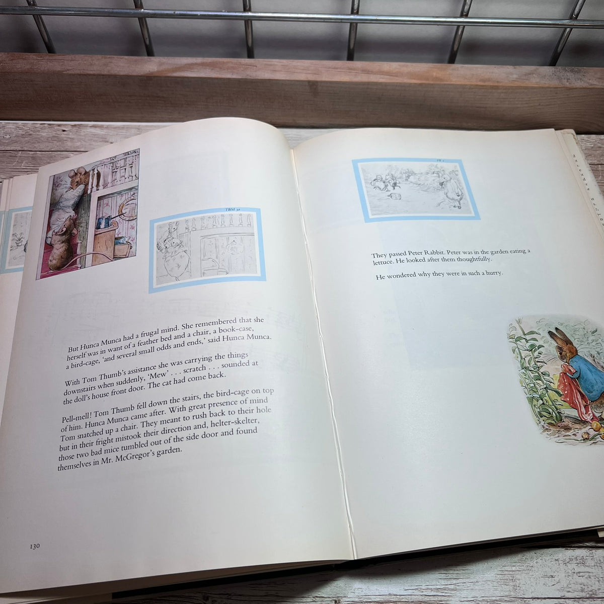 An open vintage book showing printed text and small illustrations on both pages, photographed from above on a wooden surface with a metal grid background.