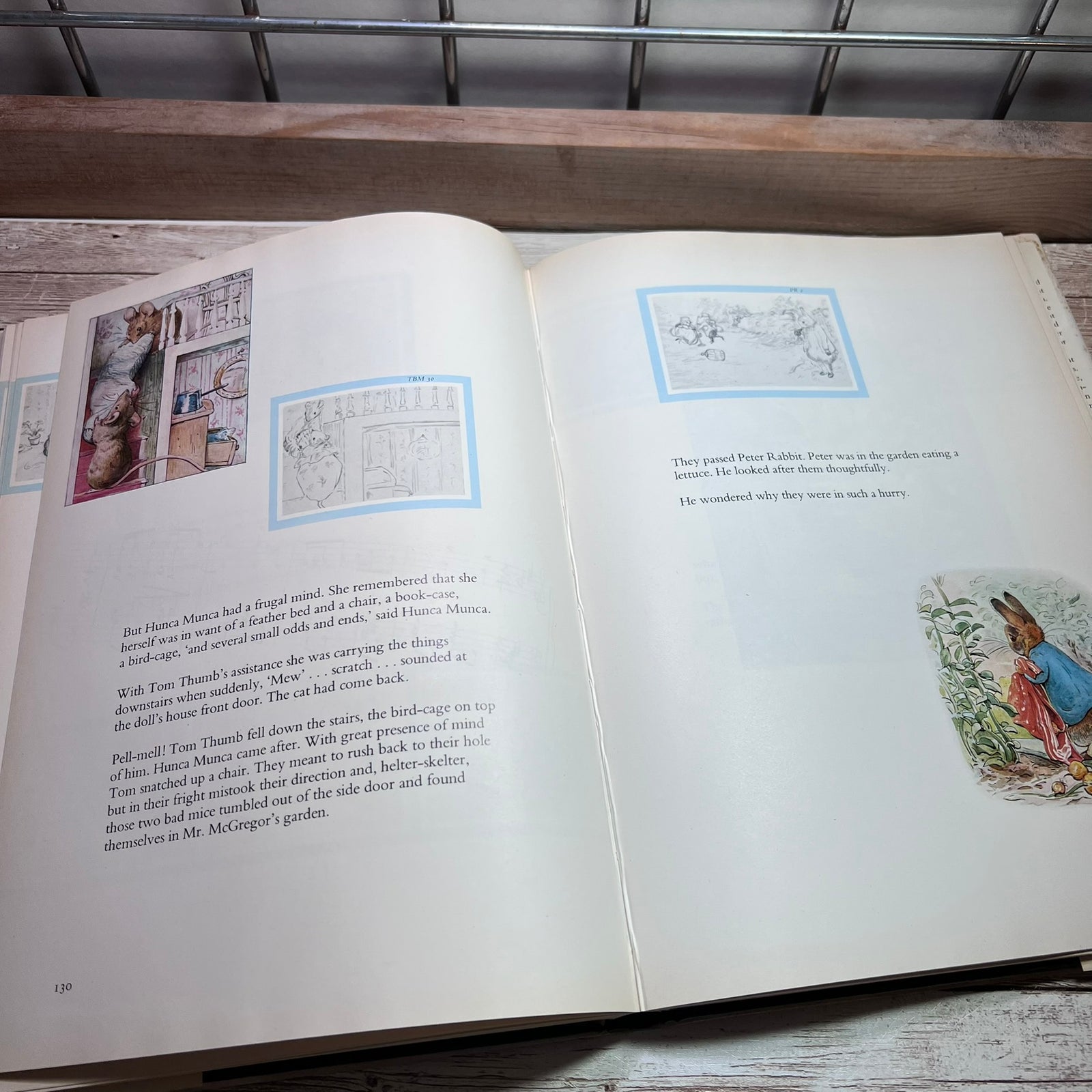 An open vintage book showing printed text and small illustrations on both pages, photographed from above on a wooden surface with a metal grid background.