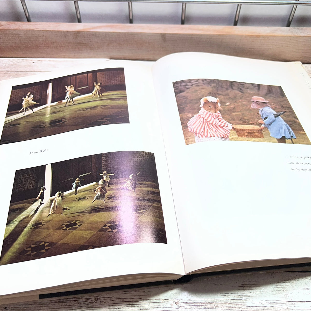An open book or photo album laid on a light wood surface, showing two printed pages with vintage photographs of dancers in motion. The left page has two small photos with caption text, and the right page has one larger photo of two people outdoors.