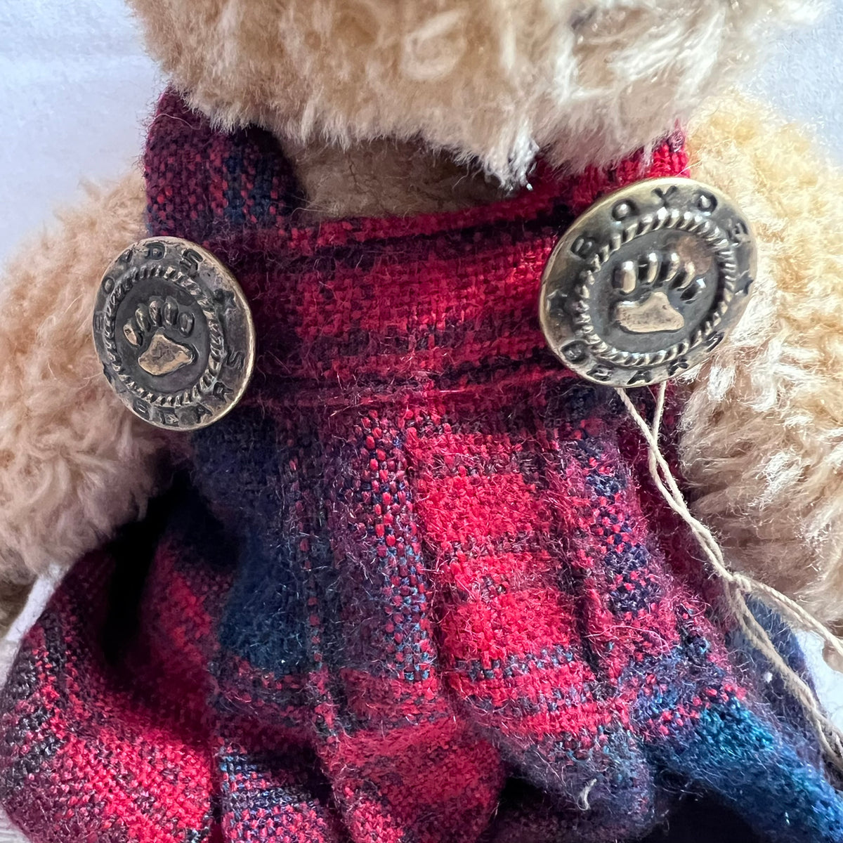 Close-up of a plush teddy bear wearing a red and navy plaid knit outfit with two decorative metal buttons featuring paw prints.