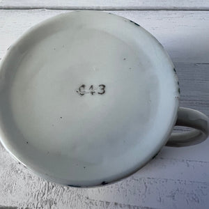 Ceramic mug with a number '043' on a light wooden surface