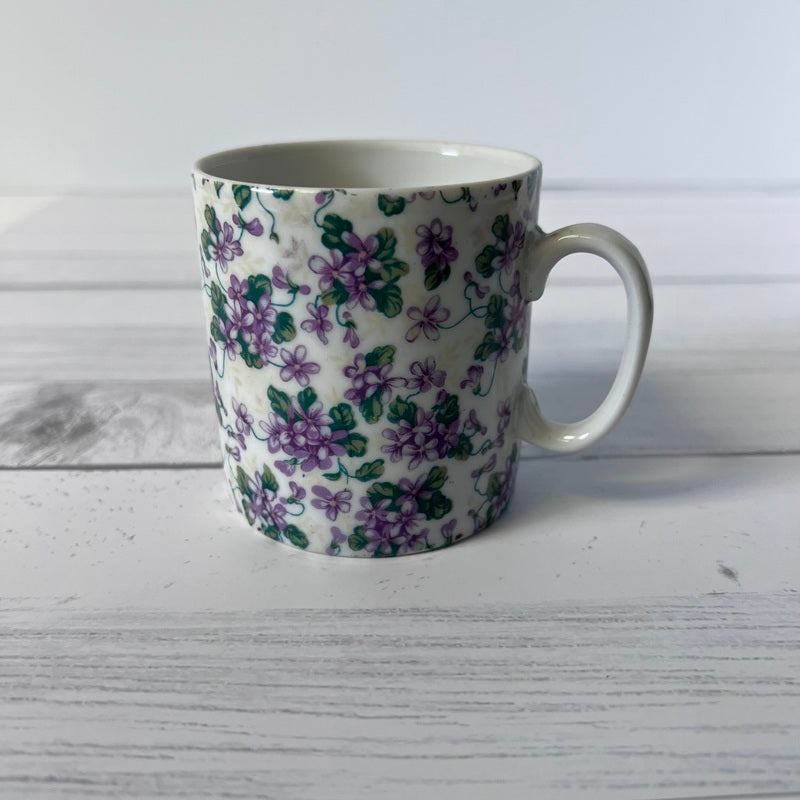 White mug with purple floral pattern on a light wooden surface