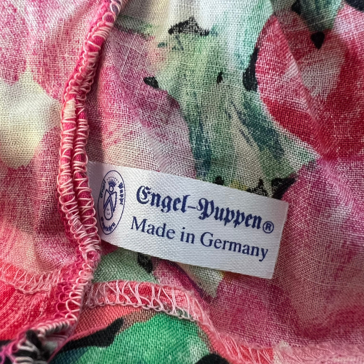 Close-up of a colorful floral fabric with a white sewn-in label reading 'Engel-Puppen Made in Germany'.
