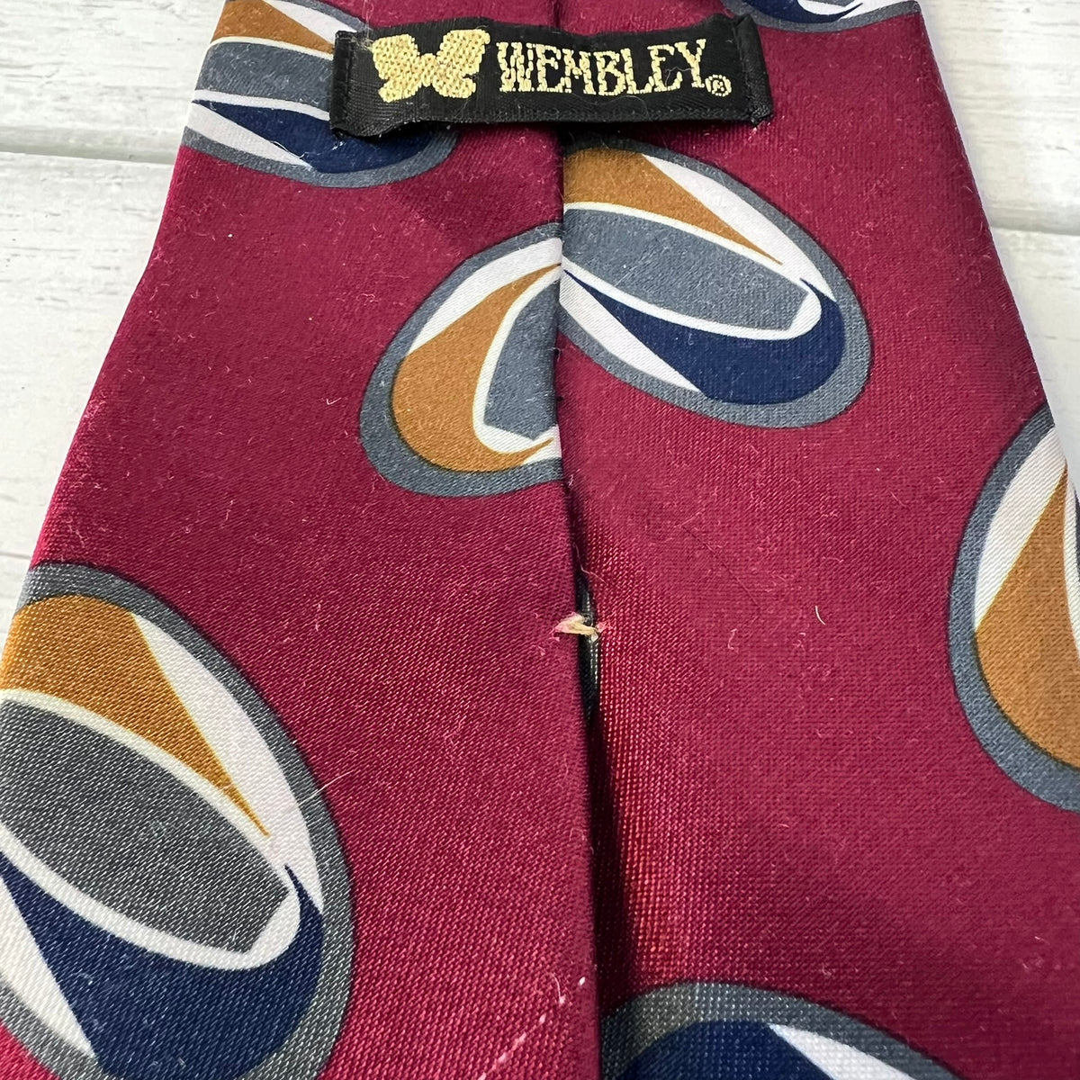 Maroon tie with multicolored circular patterns and 'Wembley' label on a wooden surface
