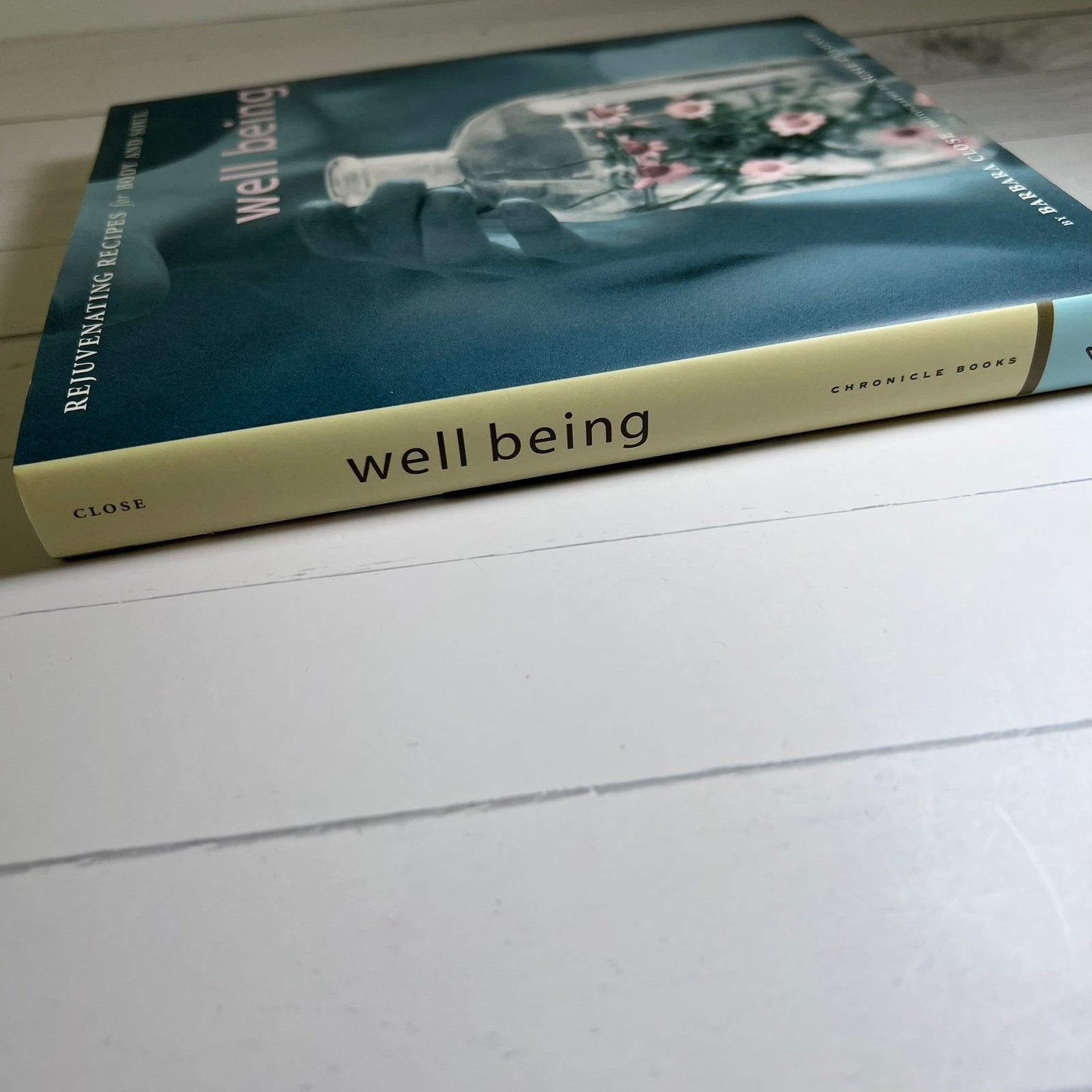 A book titled 'well being' by Dr. Wayne Dyer lies on a white wooden surface, angled diagonally.