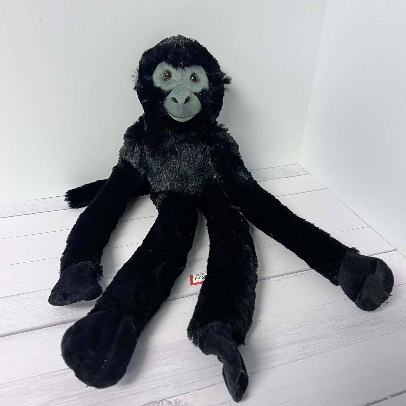 Black plush monkey toy on a white wooden floor