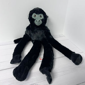Black plush monkey toy on a white wooden floor