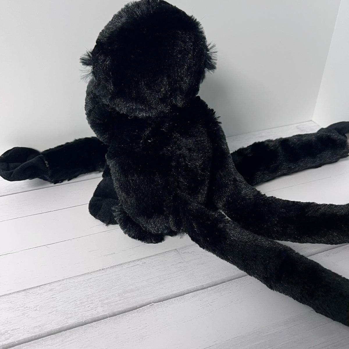 Black plush toy spider on a white wooden floor