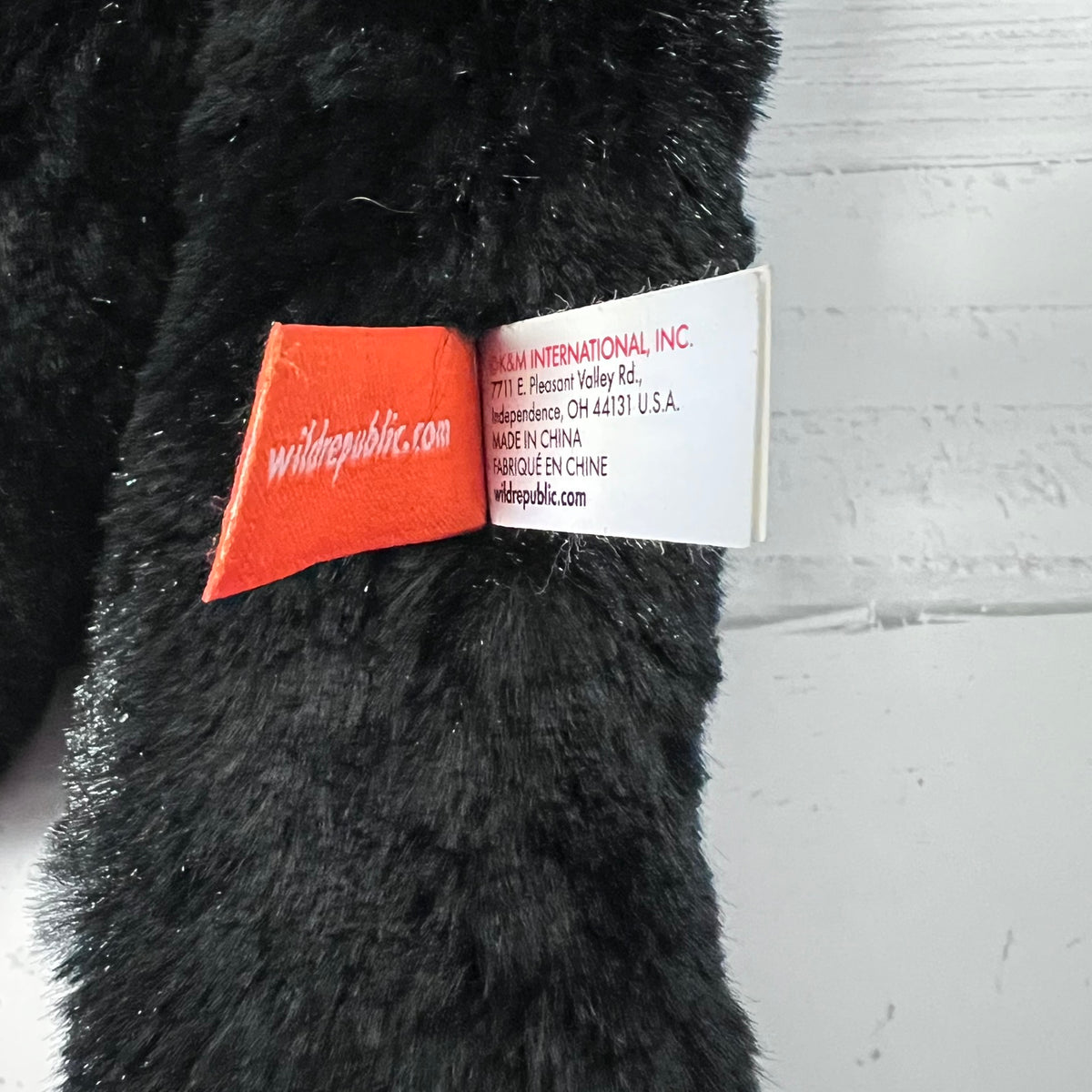 Black plush toy with a visible brand label on a gray background
