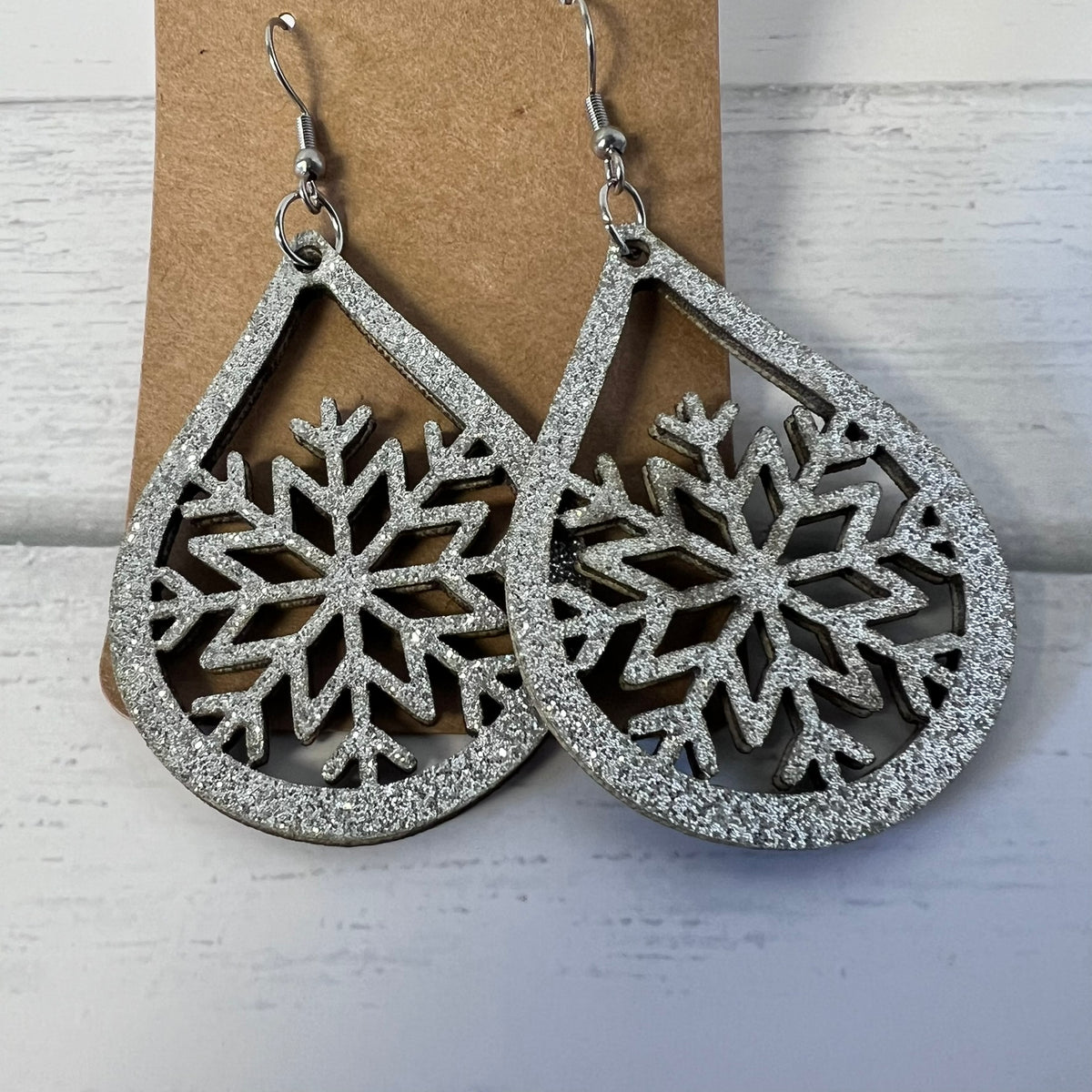 Silver snowflake earrings on a cardboard backing with a light wooden background