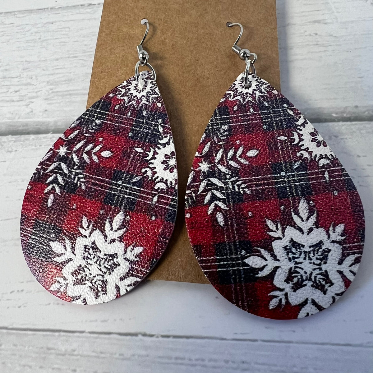 Teardrop-shaped earrings with red, black, and white pattern on a wooden background