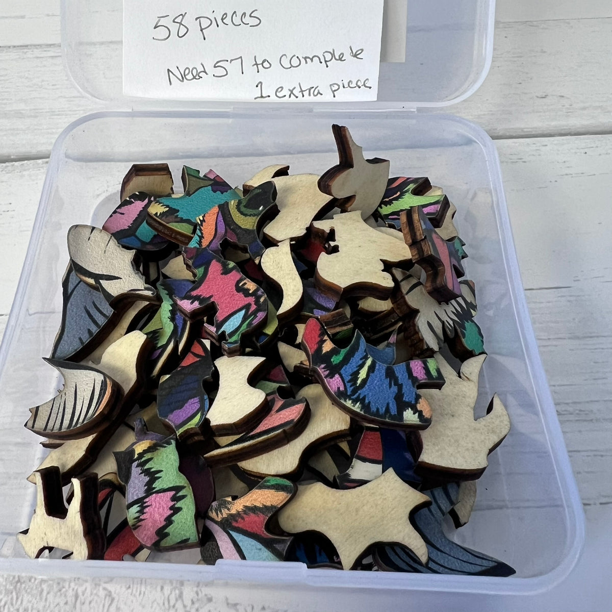 Container of colorful wooden pieces with a label indicating quantity on a white surface