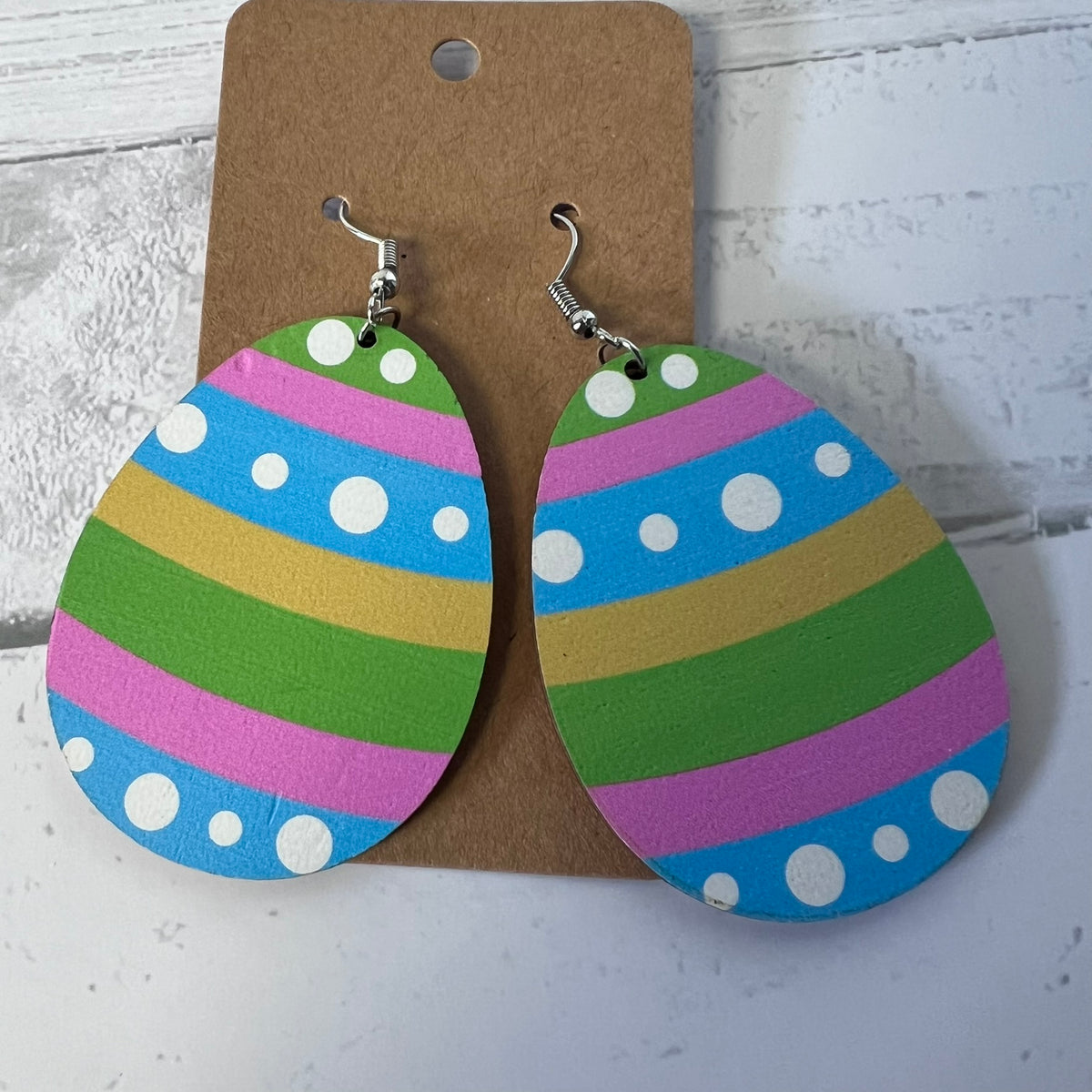 Colorful striped earrings with polka dots on a brown card against a white background