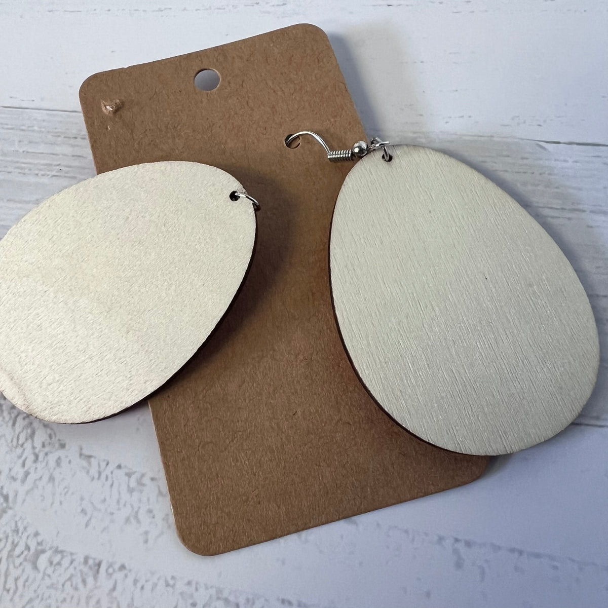 White earrings on a brown card against a light gray background