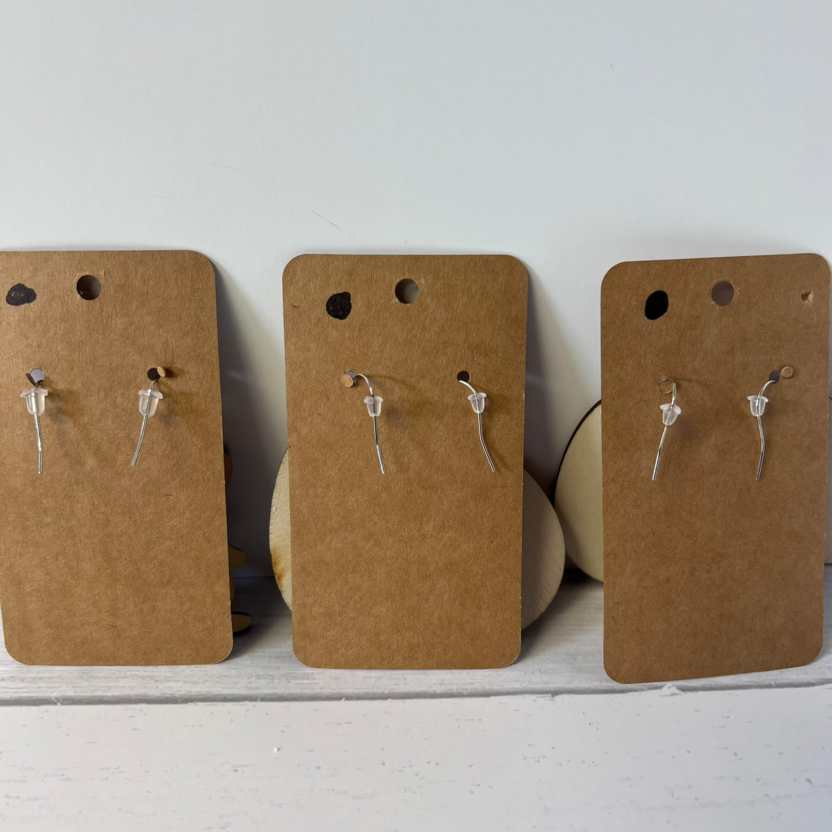 Three pairs of earrings on brown cardboard cards against a white background