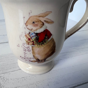 Mug with a rabbit design wearing a red coat on a light wooden surface