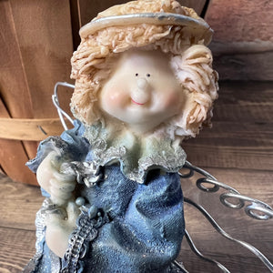 Decorative figurine with a blue dress and beige hat on a wooden surface