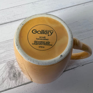 Yellow mug with 'Gallery' branding on a light wooden surface