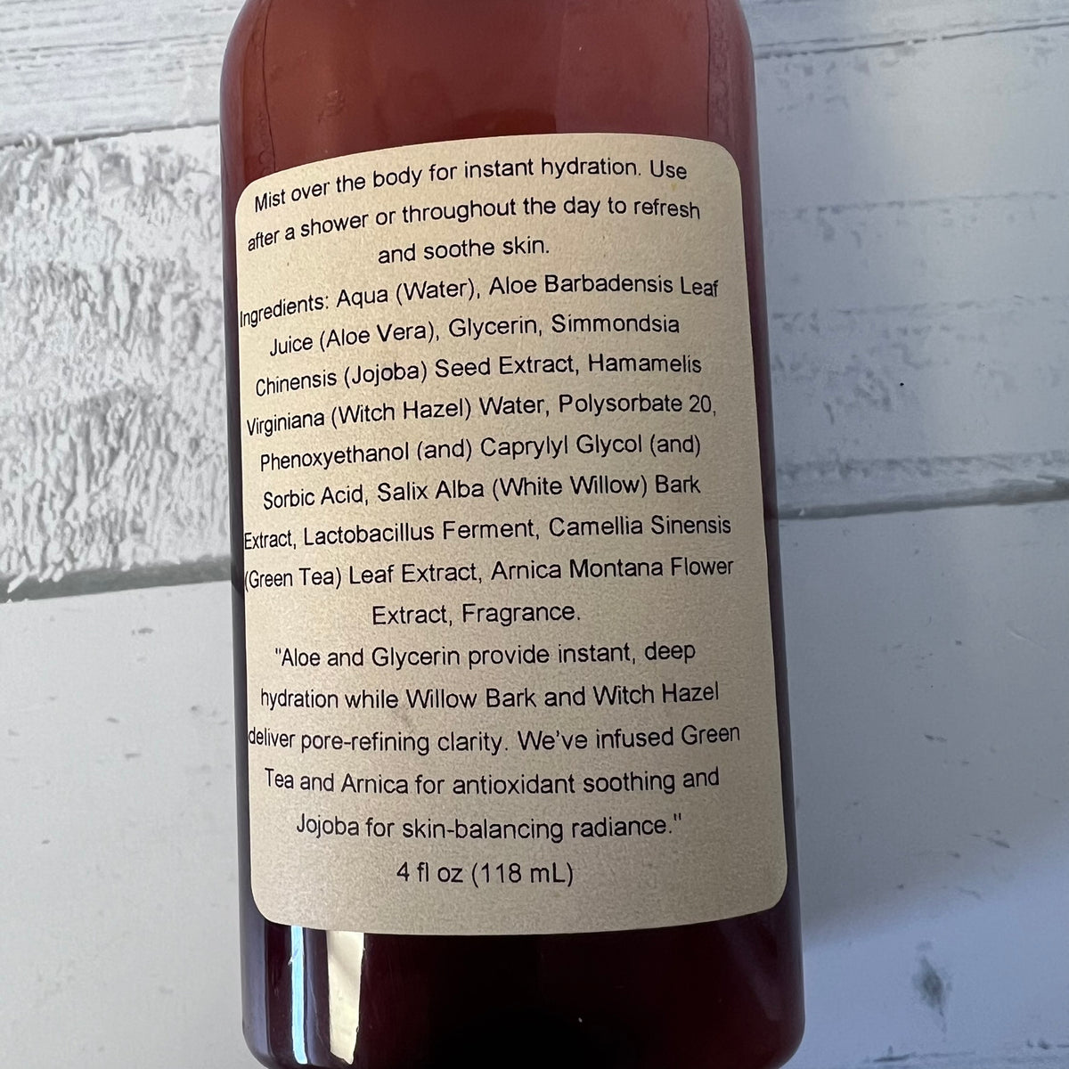 A close-up of a brown bottle showing the back label with product ingredients and usage text, photographed against a light gray textured background.