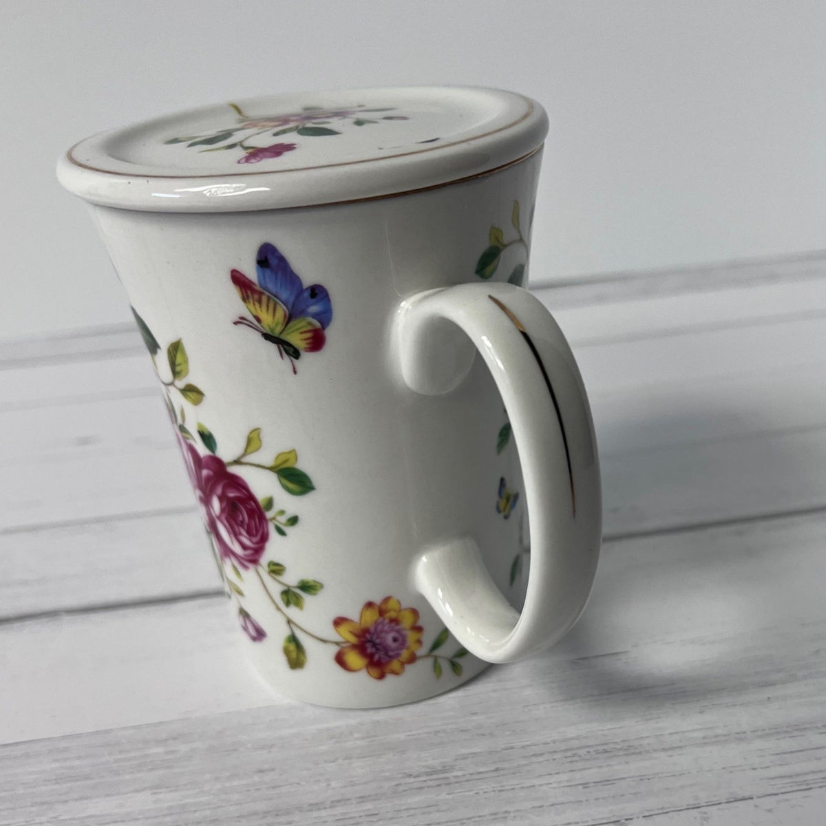 White mug with floral and butterfly design on a light wooden surface