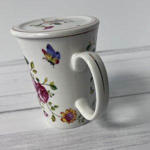 White mug with floral and butterfly design on a light wooden surface