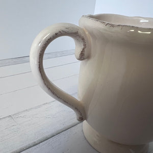White ceramic pitcher with rustic finish on a light wooden surface