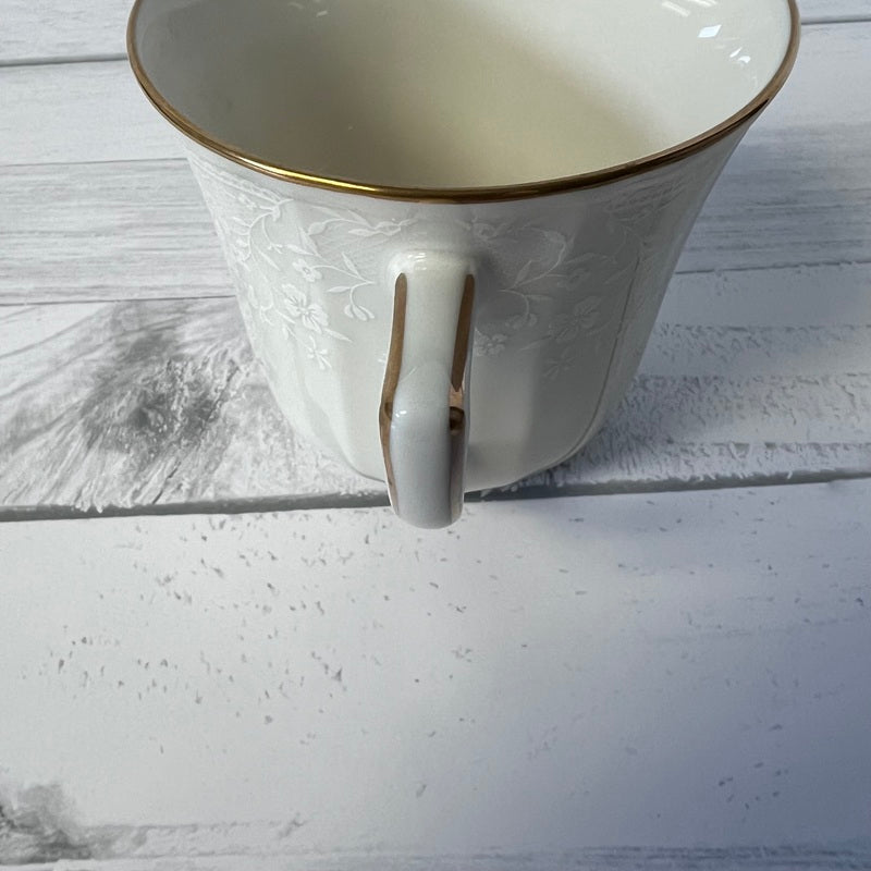 White ceramic mug with gold rim and handle on a light wooden surface