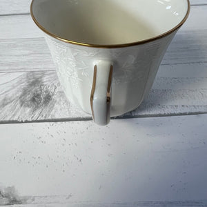 White ceramic mug with gold rim and handle on a light wooden surface