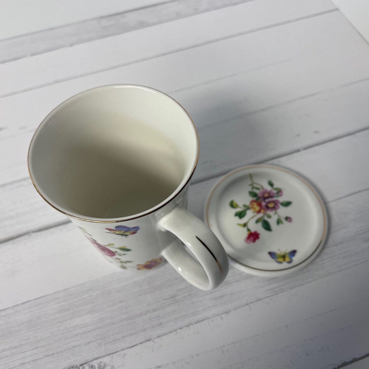 Ceramic mug and matching coaster with floral and butterfly design on a white wooden surface