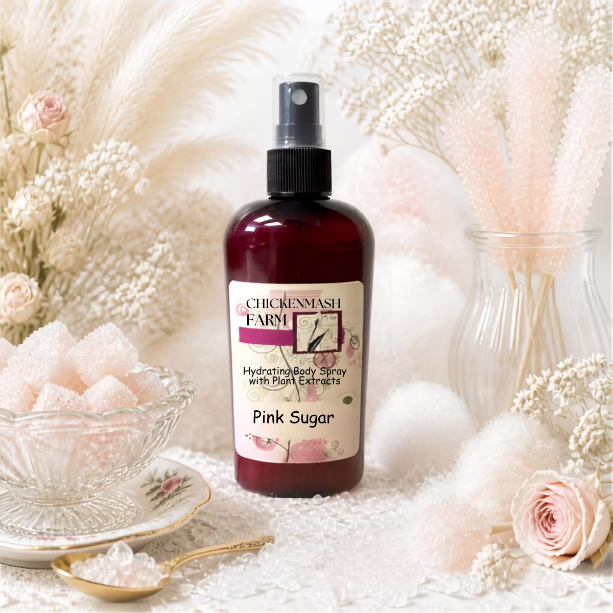 A bottle of Chickenmash Farm Pink Sugar Hydrating Body Spray with Plant Extracts, styled with pink sugar cubes, a gold spoon, and dried pampas grass in a soft, warm aesthetic.