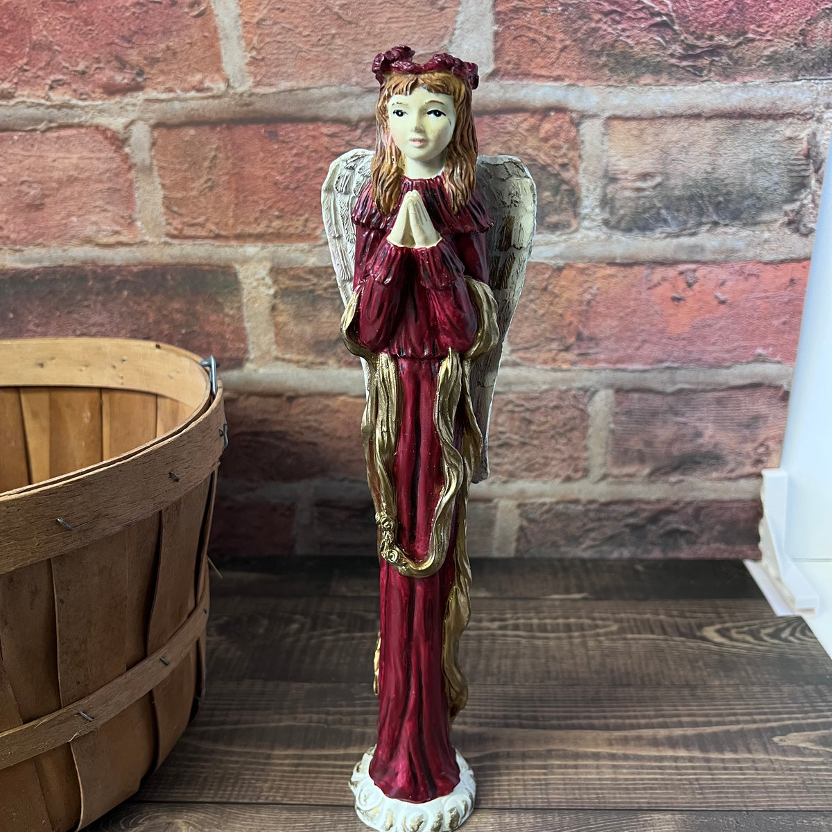 Decorative angel figurine with red and gold attire against a brick wall.