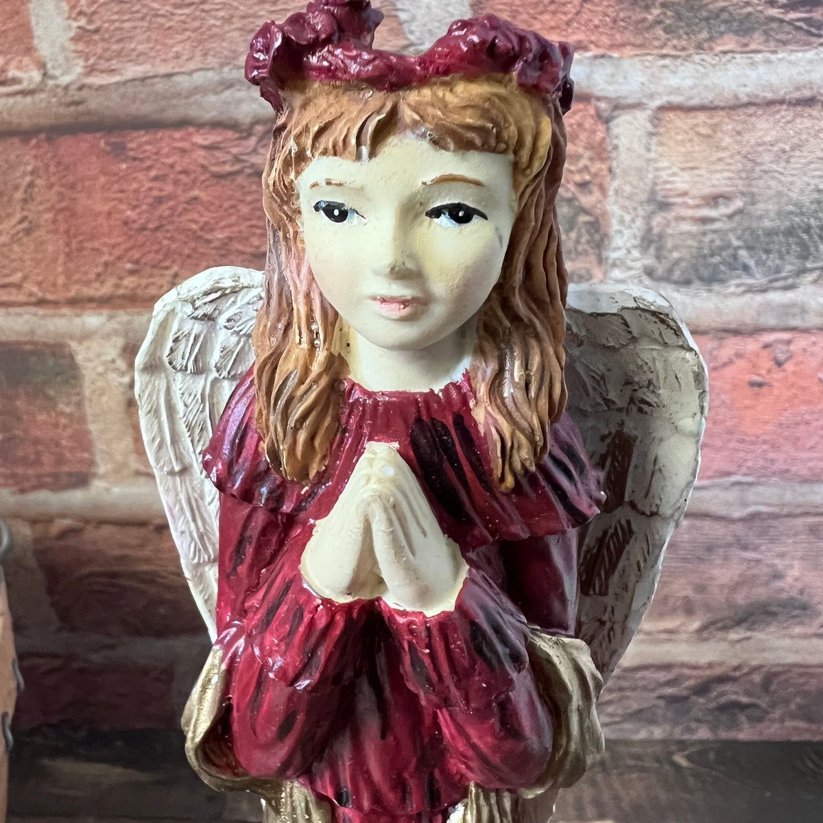 Angel figurine with red dress and red headband against a brick wall background