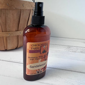 Bottle of Chickenmash Farm Sandalwood body spray on a wooden surface with a wooden basket in the background.