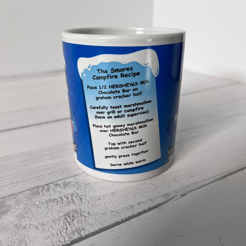 Blue mug with white interior and exterior, featuring a S'mores recipe on a light gray surface.