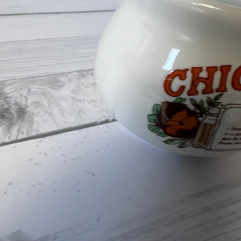 White ceramic bowl with 'Chicken soup' branding on a wooden surface